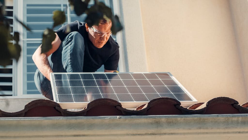 A Man in Black Shirt Installing a Solar Panel on the Roof